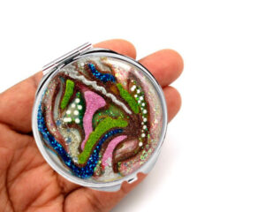 Compact mirror laying on a woman's hand to show the size. Designed by Terlis Designs.