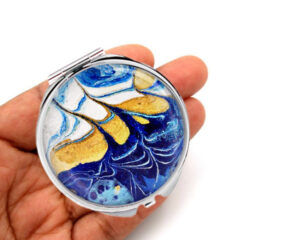 Cosmetic pocket mirror laying on a woman's hand to show the size. Designed by Terlis Designs.