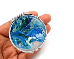 Custom cosmetic handheld mirror laying on a woman's hand to show the size. Designed by Terlis Designs.