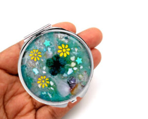 Custom floral handheld mirror laying on a woman's hand to show the size. Designed by Terlis Designs.