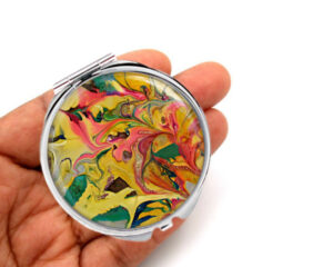 Custom metal compact mirror laying on a woman's hand to show the size. Designed by Terlis Designs.