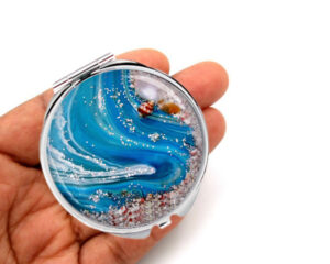 Custom round compact mirror laying on a woman's hand to show the size. Designed by Terlis Designs.