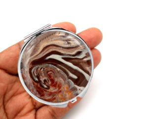 Custom round handheld mirror laying on a woman's hand to show the size. Designed by Terlis Designs.