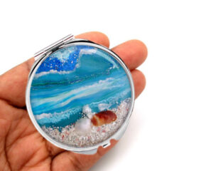 Double sided pocket mirror laying on a woman's hand to show the size. Designed by Terlis Designs.