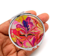 Ocean art compact mirror laying on a woman's hand to show the size. Designed by Terlis Designs.