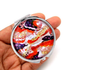 Portable compact mirror laying on a woman's hand to show the size. Designed by Terlis Designs.