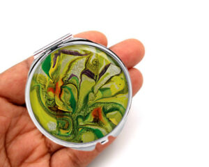 Portable pocket mirror laying on a woman's hand to show the size. Designed by Terlis Designs.