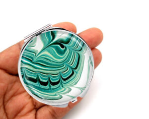 Seafoam green handheld mirror laying on a woman's hand to show the size. Designed by Terlis Designs.