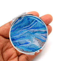 Silver compact mirror laying on a woman's hand to show the size. Designed by Terlis Designs.