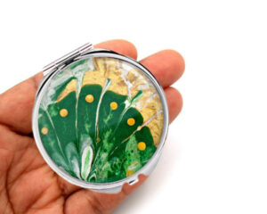 Travel compact mirror laying on a woman's hand to show the size. Designed by Terlis Designs.
