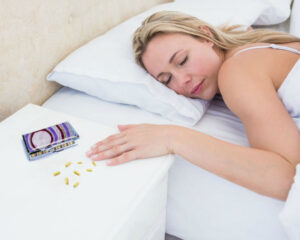 Vitamin Pill Box - PILB114, placed on a bedside table, with a woman peacefully sleeping in her bed, by Terlis Designs